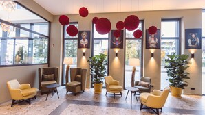 A lobby with multiple seating areas, large windows, and decorative red spheres. - Hotel Libertas elements pure (Merzhausen)