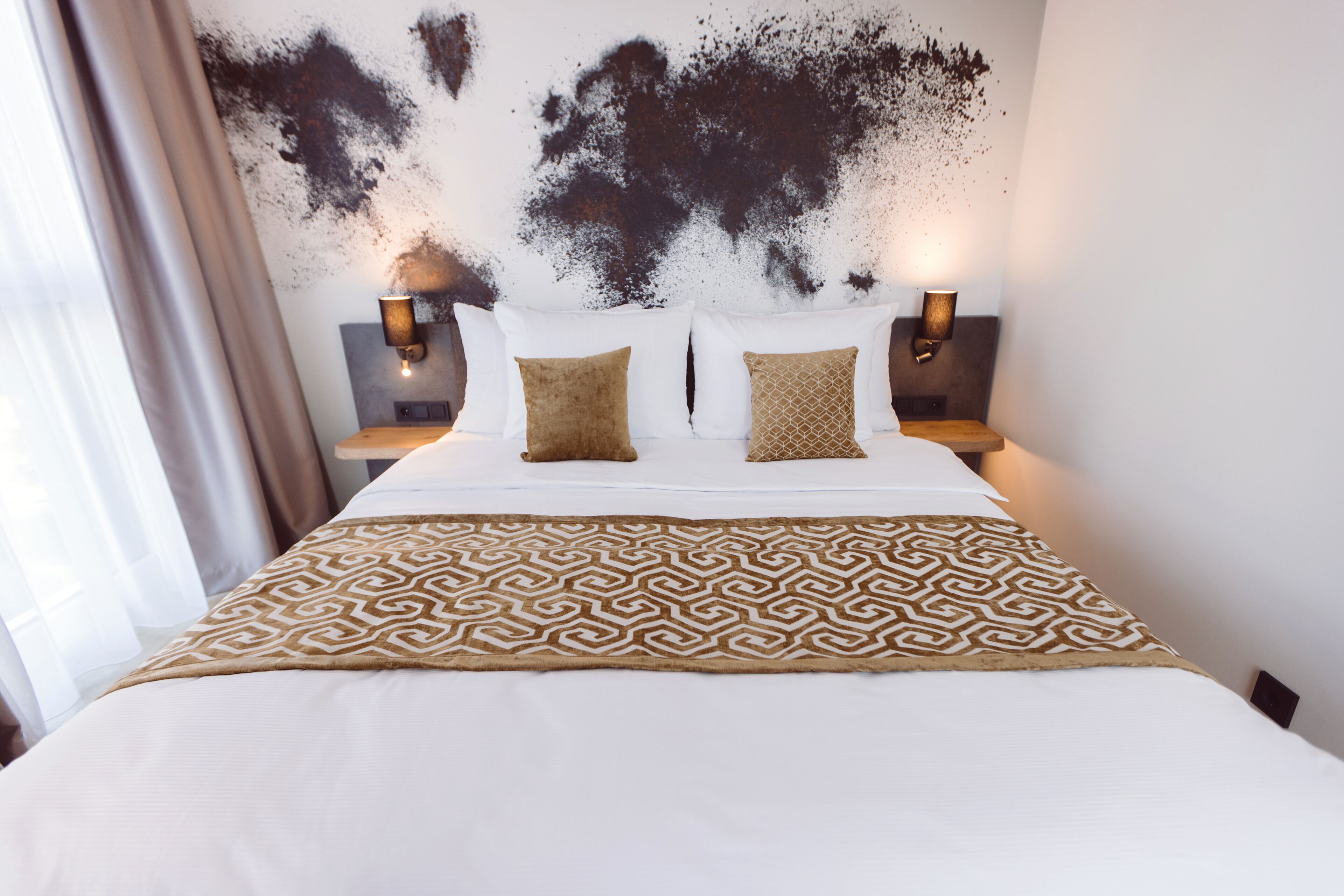 A hotel room with a large bed, two bedside lamps, and a patterned throw blanket.