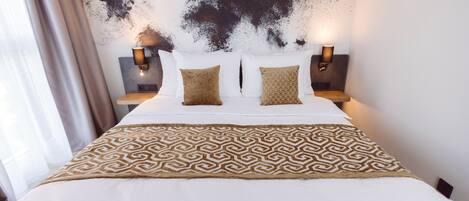 A hotel room with a large bed, two bedside lamps, and a patterned throw blanket.