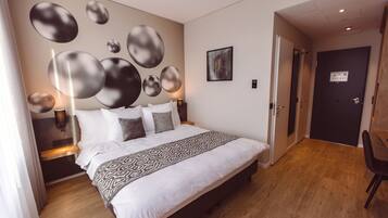 A modern hotel room with a large bed, a wall-mounted abstract art piece, and a door leading to another room.