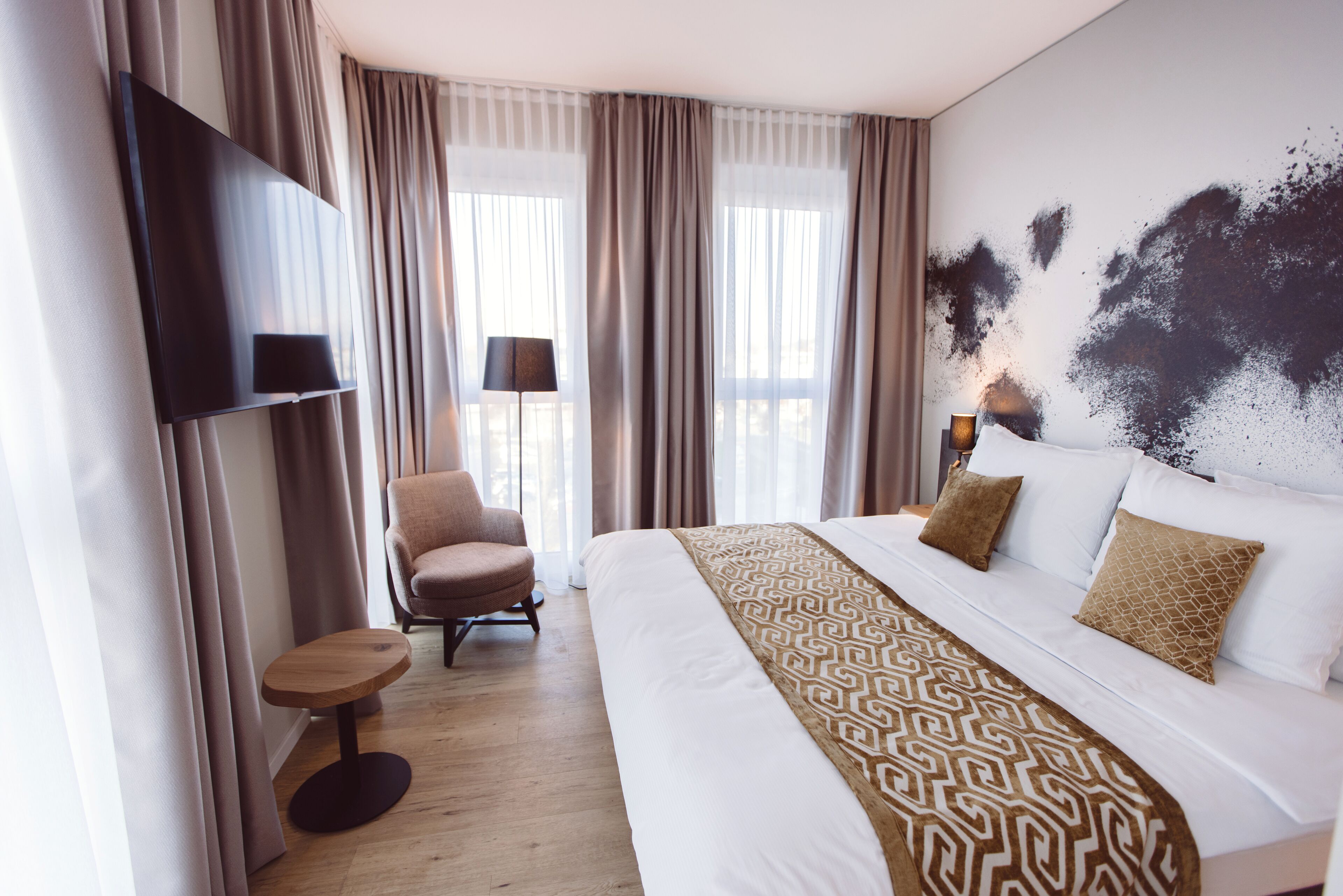 Et hotelværelse med en seng, en stol, et lille bord og et fjernsyn ophængt på væggen.