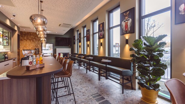 A modern bar area with a bar counter, seating, and a large potted plant. - Hotel Libertas elements pure (Merzhausen)