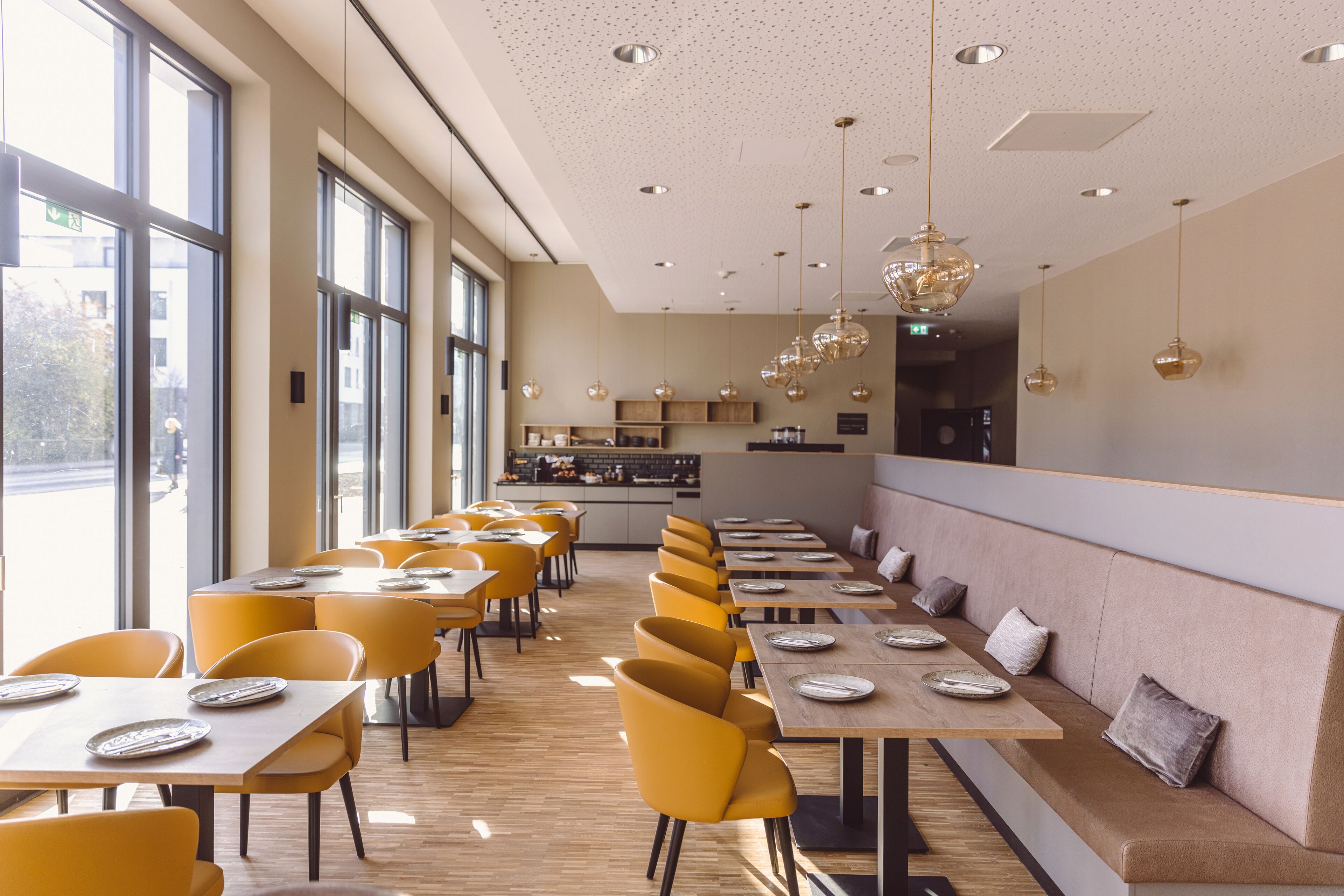 A modern restaurant with yellow chairs, wooden tables, and pendant lighting.