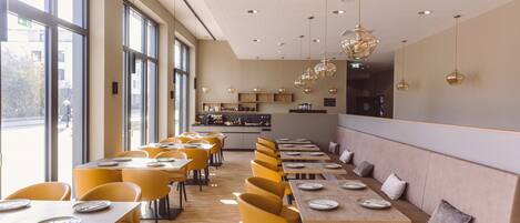 A modern restaurant with yellow chairs, wooden tables, and pendant lighting.