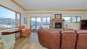 A spacious living room with a fireplace, leather sofas, and a view of a snowy landscape through large windows. - Top-Floor Ski-In/Out Condo with Fireplace, Mountain Views & Peloton Access.Close (Big Sky)