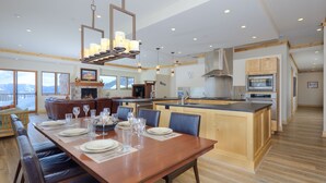A spacious dining area with a wooden table set for a meal, a fireplace, and a view of the mountains. - Top-Floor Ski-In/Out Condo with Fireplace, Mountain Views & Peloton Access.Close (Big Sky)
