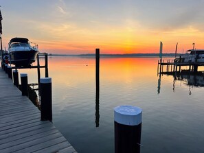 A calm waterfront with docked boats, a wooden pier, and a sunset.