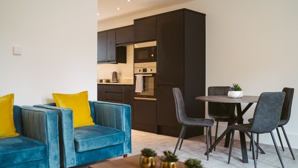 Una sala de estar moderna con un sofá azul, una mesa de centro de madera y un comedor con una mesa redonda y sillas.