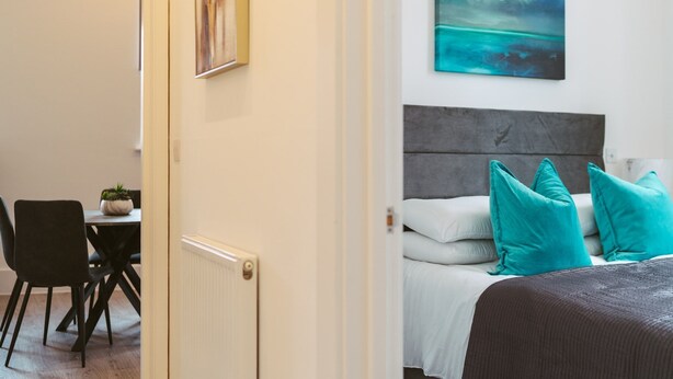 A hotel room with a bed, a headboard, and a painting on the wall. - York Riverside Apartments are 11 beautiful, modern, and stylish apartments based in the centre of Hi (York)