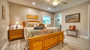Un dormitorio con cama de madera, una mesita de noche, lámpara, ventilador de techo, ventana y puerta.