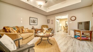 Una sala de estar con sofá, mesa de centro y mueble para televisión. Se ve un comedor con mesa y sillas al fondo.