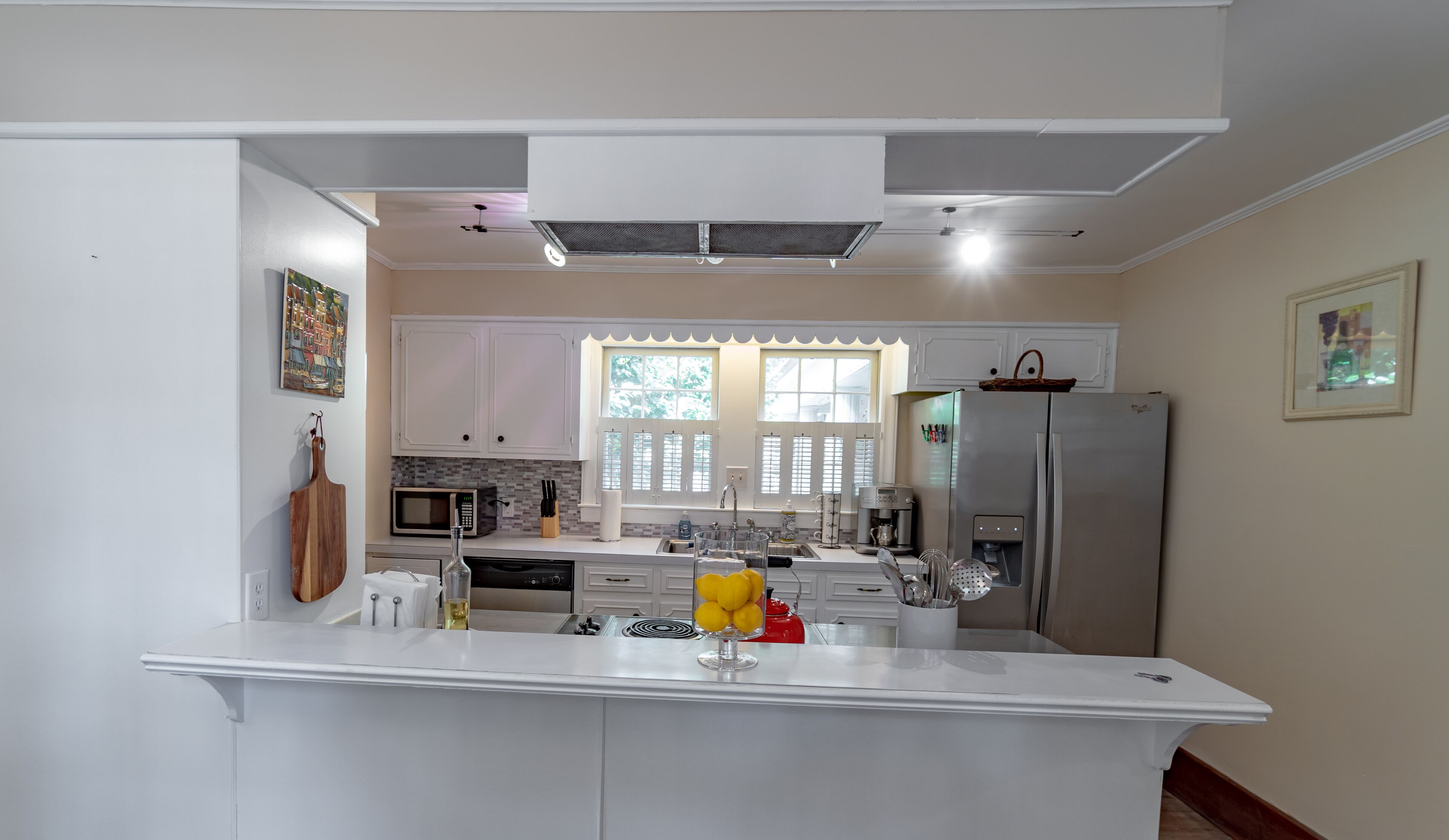 A modern kitchen with white cabinetry, a central island, a microwave, a refrigerator, and a window with blinds.