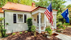 Una casa blanca con techo rojo, un porche y dos banderas.