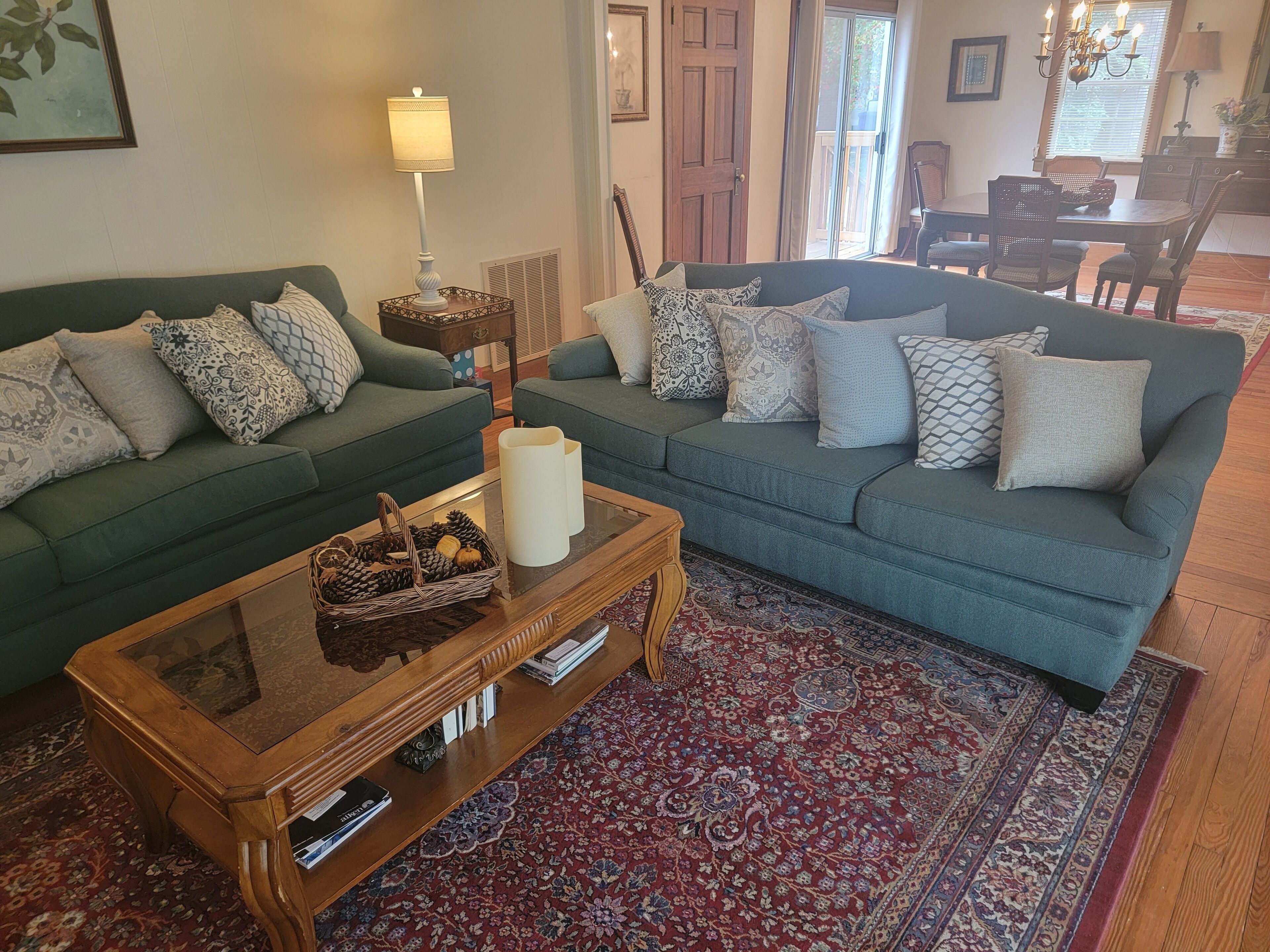 A living room with two green sofas, patterned cushions, a wooden coffee table, and a red patterned rug.