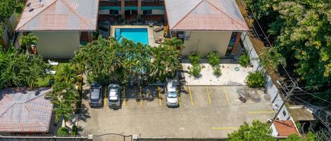 An aerial view of a hotel with a swimming pool, multiple parking spaces, and lush greenery.
