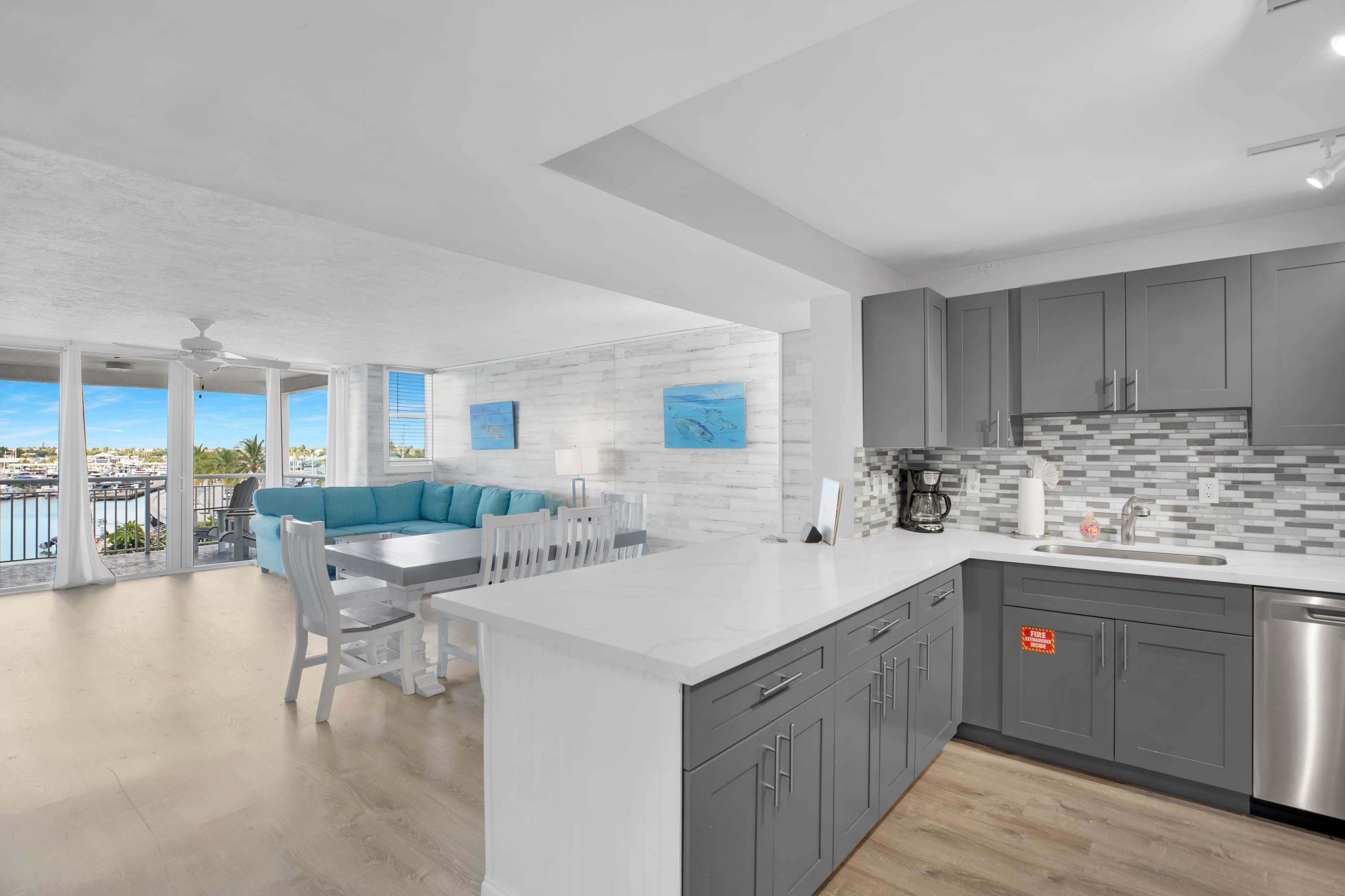 A modern kitchen with grey cabinets, a white countertop, and a view of the marina.