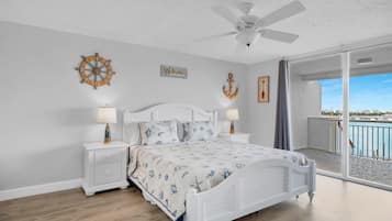 A bedroom with a bed, nightstands, a ceiling fan, and a view of the sea through a sliding glass door.