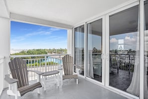 A balcony with two Adirondack chairs and a small table, overlooking a pool and a view of the city skyline.