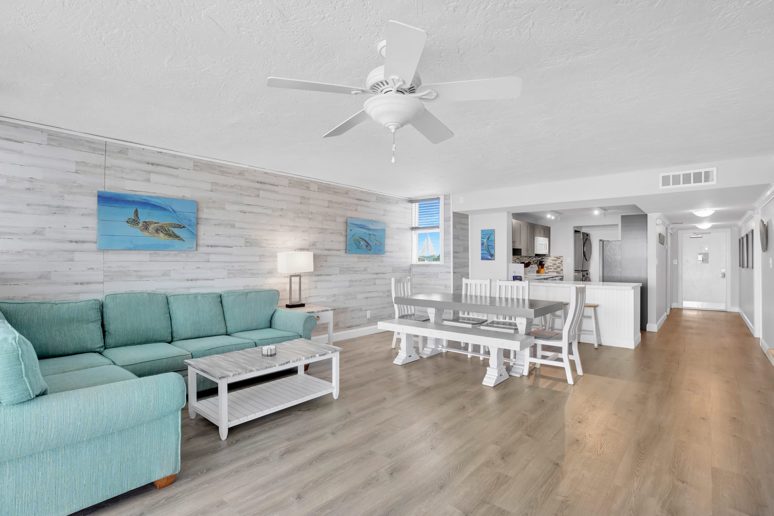 A spacious living room with a teal sofa, a white coffee table, and a dining area with a white table and chairs.