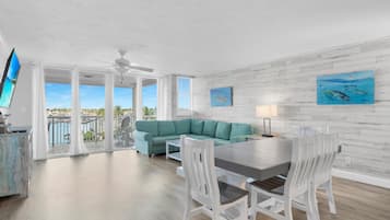 A modern living room with a teal sofa, white chairs, a dining table, and artwork on the walls.