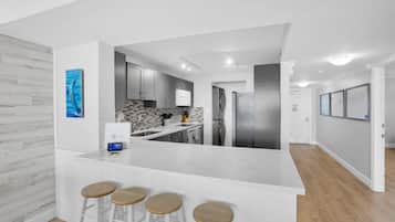 A modern kitchen with a white island, bar stools, and a view into the dining area.