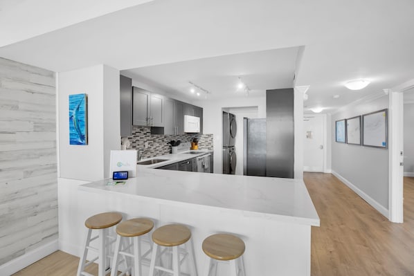 A modern kitchen with a white island, bar stools, and a view into the dining area.