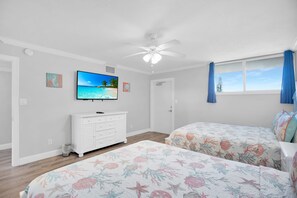 A bedroom with two beds, a ceiling fan, a TV, and a window with curtains.