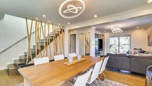 A modern living room with a wooden dining table, white chairs, a grey sofa, and a staircase with bamboo decor. - Near Yale & Lighthouse Point Beach: Home w/ Pool! (New Haven)