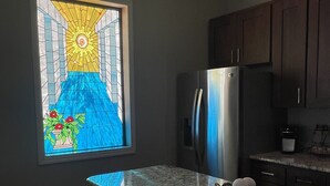 Una cocina con encimera de granito, refrigerador de acero inoxidable, gabinetes de madera oscura y un ventanal con diseño de sol.