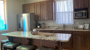 Una cocina moderna con encimera de granito, armarios de madera oscura, electrodomésticos de acero inoxidable y una zona con taburetes de bar.