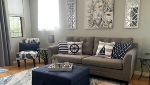 Una sala de estar con un sofá gris, un reposapiés azul y una alfombra estampada.