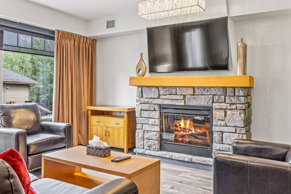 A modern living room with a stone fireplace, leather furniture, and a large flat-screen TV.