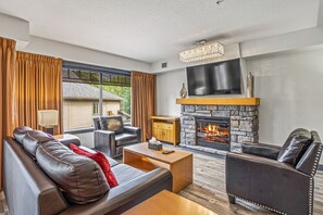 Een moderne woonkamer met lederen meubels, een stenen openhaard en een groot raam met gordijnen.