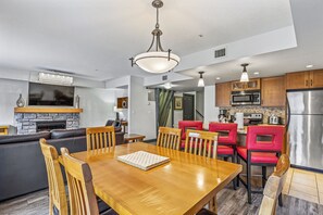 A modern kitchen with a central island, wooden dining table, and red bar stools.