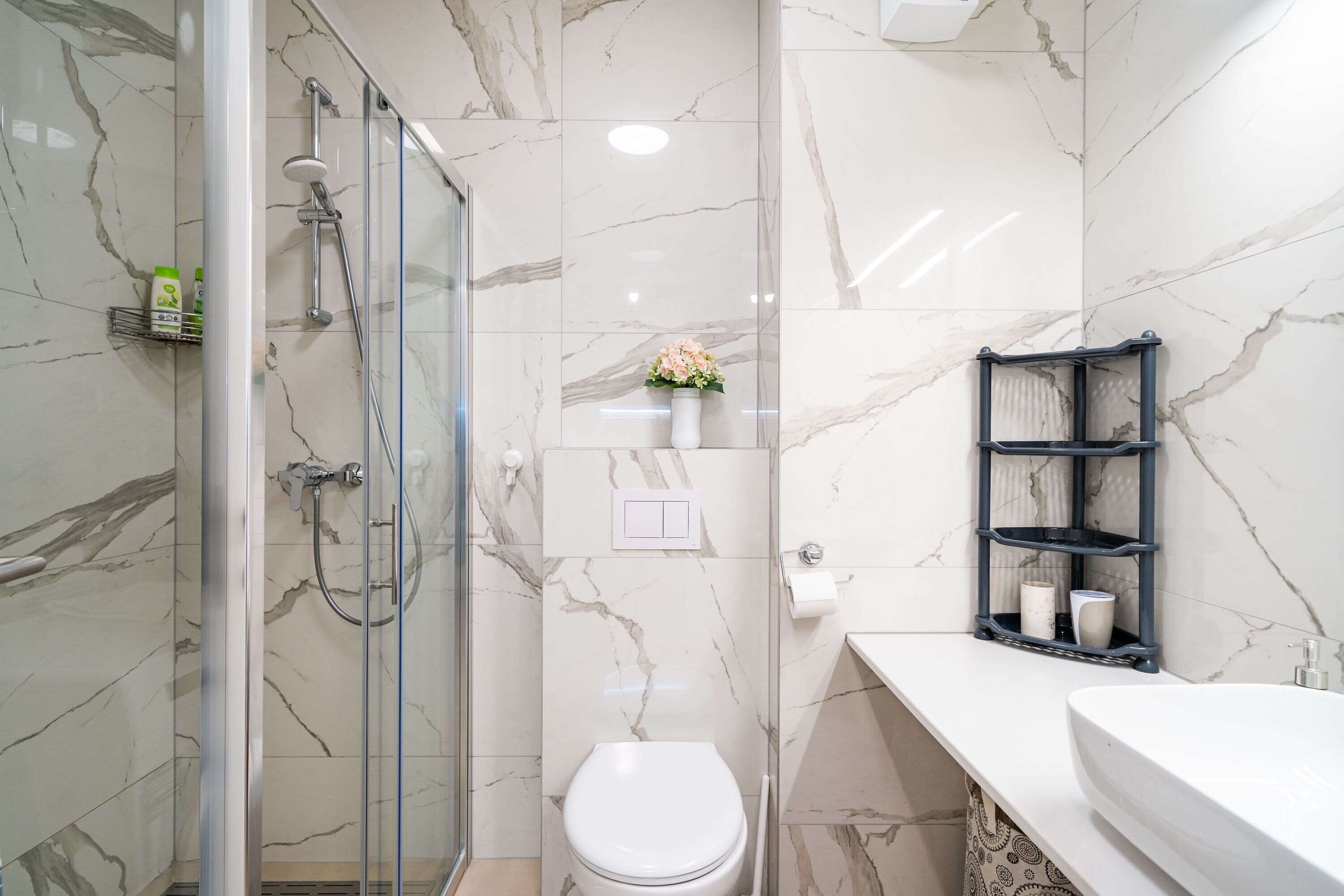 Ein modernes Badezimmer mit einer gläsernen Duschkabine, einer weißen Toilette und einer Marmor-Spritzschutzwand.