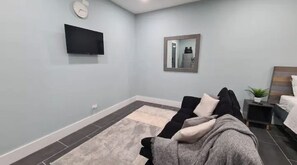 Relax in a comfortable space with a flat-screen TV, large mirror, and a neatly made bed.
