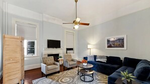 A living room with a fireplace, two armchairs, a sofa, a coffee table, and a ceiling fan. - Lanaux Mansion - Beth's Escape with Courtyard Balcony (New Orleans)