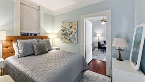 A bedroom with a large bed, bedside lamps, a painting, and a view into a living area. - Lanaux Mansion - Beth's Escape with Courtyard Balcony (New Orleans)