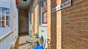 A narrow outdoor corridor with a brick wall, a welcome sign to the porch, a small table with chairs, and a blue chair. - Lanaux Mansion - Beth's Escape with Courtyard Balcony (New Orleans)