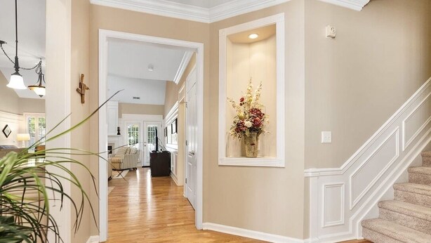 A hallway with wooden flooring, a staircase, and a wall-mounted flower arrangement. - Spacious & Private Getaway Near Downtown Raleigh! (Raleigh)