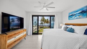 Un dormitorio con cama, televisor, ventilador de techo y una pintura.