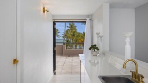 Una cocina moderna con vista al océano, un balcón con palmeras y una decoración en tonos blancos.