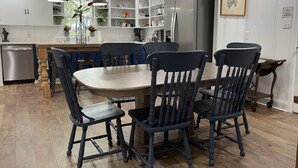 A modern kitchen with white cabinetry, a stainless steel refrigerator, and a dining area with a wooden table and dark chairs. - The Fox Den, luxury home, just 2 minutes away from the iconic Bell Buckle Cafe. (Bell Buckle)