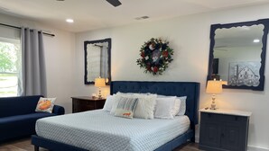 A bedroom with a large bed, a nightstand, a dresser, a sofa, and a wall-mounted mirror. - The Fox Den, luxury home, just 2 minutes away from the iconic Bell Buckle Cafe. (Bell Buckle)