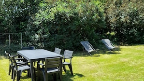An outdoor seating area with a table and chairs, surrounded by a grassy lawn and dense foliage. - Breton house 400m from the beach (Crozon)