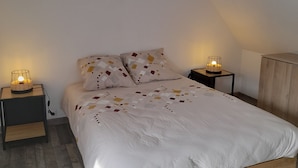 A bedroom with a sloped ceiling, a wooden bed frame, a white duvet, patterned pillows, two bedside tables with lamps, and a wooden wardrobe. - Breton house 400m from the beach (Crozon)