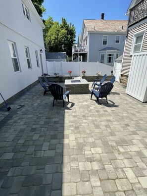 Eine Terrasse mit Steinpflasterung, Gartenmöbeln und einem Feuerkorb.