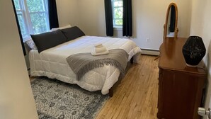 A bedroom with a bed, a ceiling fan, a wooden dresser, a rug, and a window with curtains. - Close to everything (Newport)