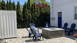 A patio area with outdoor seating, a stone fire pit, and a white building in the background. - Close to everything (Newport)