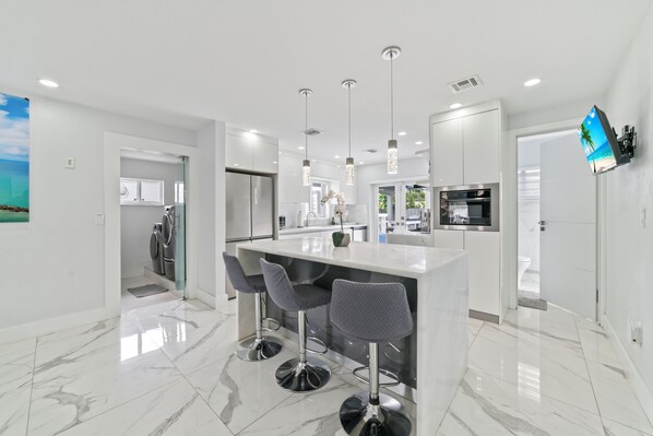 A modern kitchen with a central island, bar stools, stainless steel appliances, and pendant lighting.